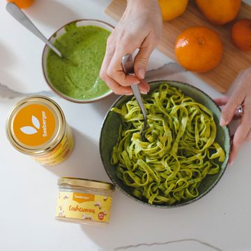 Bild eines Nudelgerichts mit grüner Pesto, daneben zwei Seeberger Produkte. Eins davon das Seeberger Cashewmus.