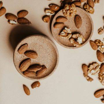 Mandeln und Walnüsse liegen auf zwei Schalen, umgeben von verstreuten Nüssen.