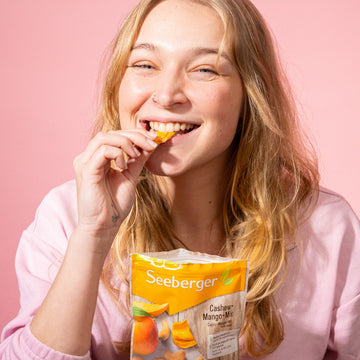 Frau isst ein Stück getrockneter Mango aus der Seeberger Produktpackung Cashew-Mango-Mix.